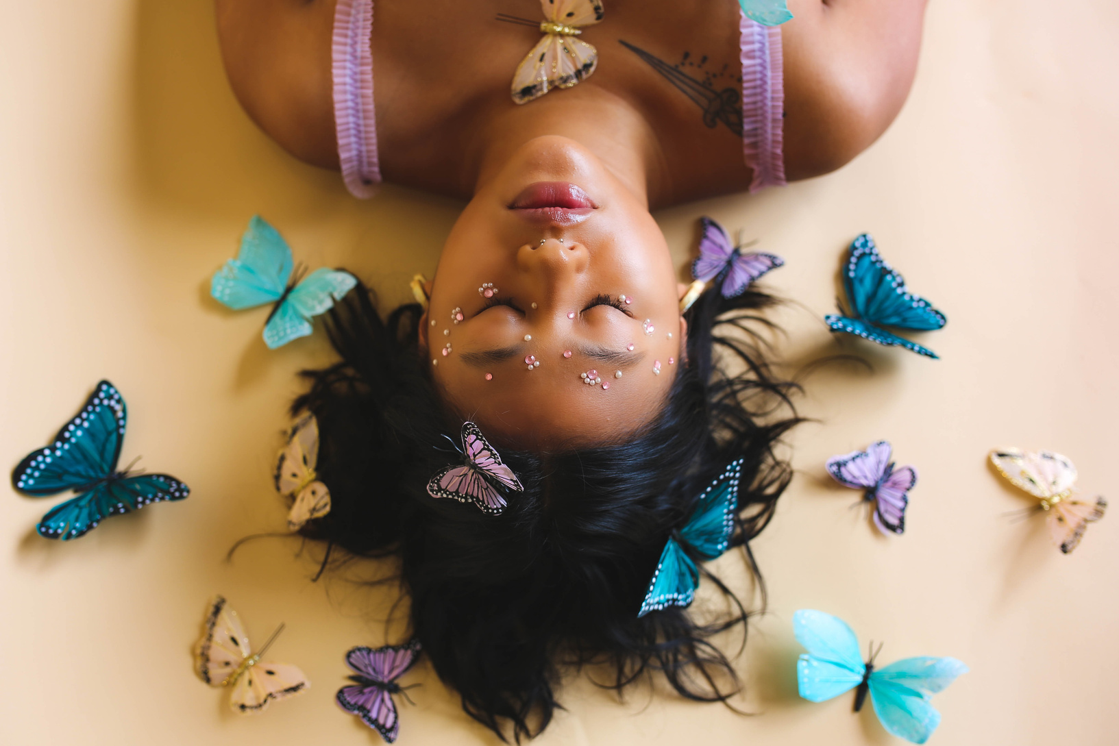 Woman with Face Stickers Lying on Beige Background with Butterflies